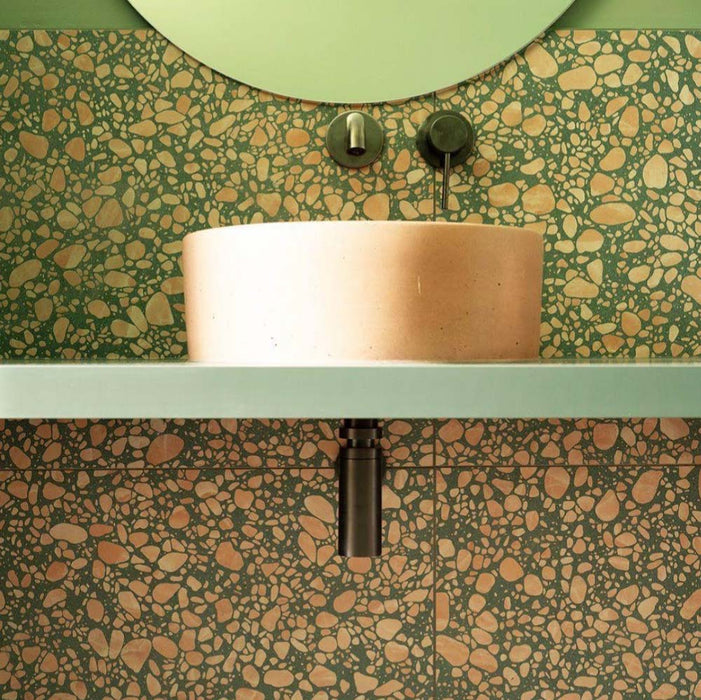 Bathroom featuring Chunks POP Terrazzo Green 60 × 60cm terrazzo-effect porcelain wall and floor tiles, paired with a curved stone basin, sage green vanity shelf, and dark brass fittings for a bold contemporary look.