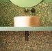 Bathroom featuring Chunks POP Terrazzo Green 60 × 60cm terrazzo-effect porcelain wall and floor tiles, paired with a curved stone basin, sage green vanity shelf, and dark brass fittings for a bold contemporary look.