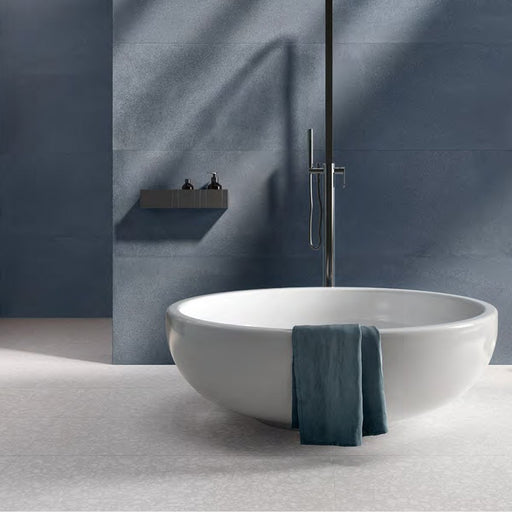 Minimalist bathroom featuring Chunks POP Terrazzo White 60 × 60cm terrazzo-effect porcelain floor tiles, paired with deep blue wall tiles, a sculptural freestanding bath, and soft natural lighting for a calm contemporary feel.