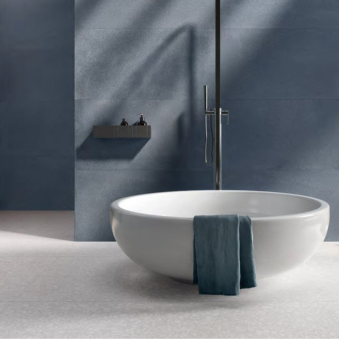 Minimalist bathroom featuring Chunks POP Terrazzo White 60 × 60cm terrazzo-effect porcelain floor tiles, paired with deep blue wall tiles, a sculptural freestanding bath, and soft natural lighting for a calm contemporary feel.