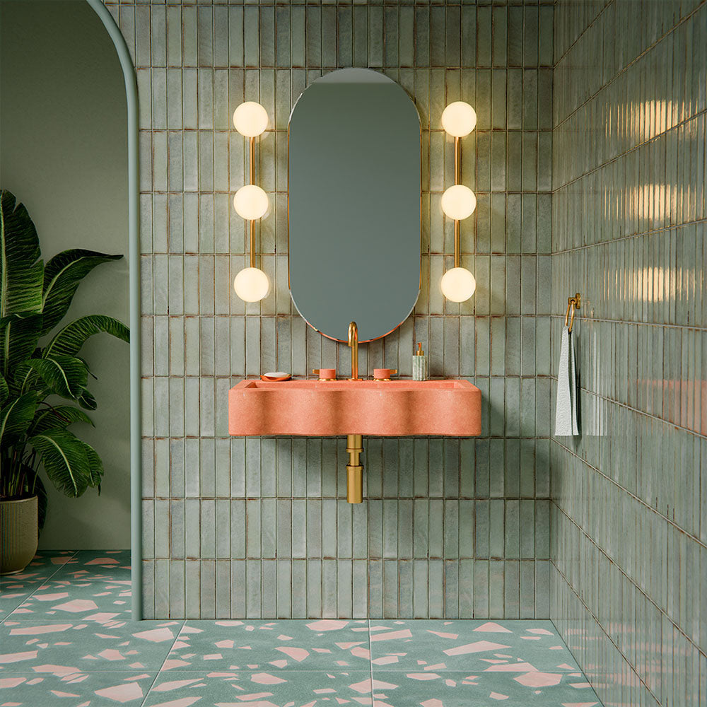 Bathroom featuring Chunks ROCK Terrazzo Green 60 × 60cm terrazzo-effect porcelain floor tiles, paired with glossy sage green wall tiles, a pink stone basin, brass fittings, and soft globe wall lighting.