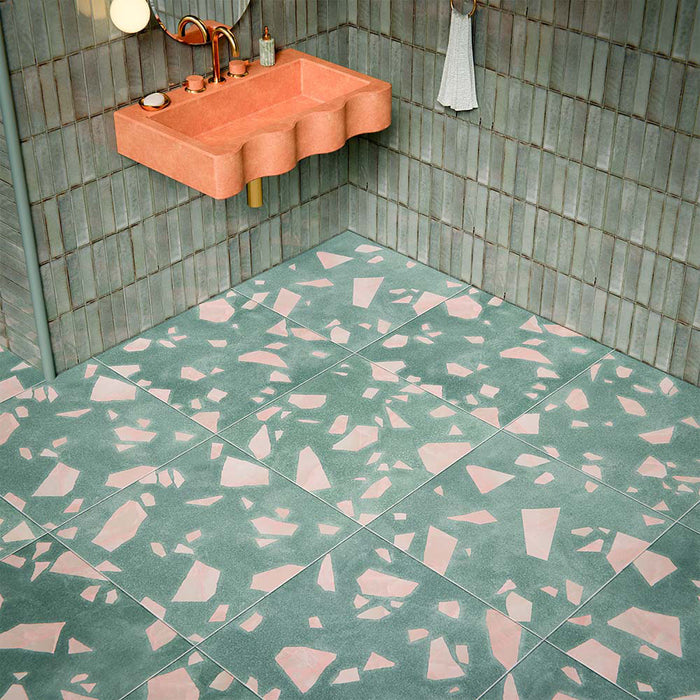 Bathroom featuring Chunks ROCK Terrazzo Green 60 × 60cm terrazzo-effect porcelain floor tiles, paired with glossy sage green wall tiles, a pink stone basin, brass fittings, and soft globe wall lighting.