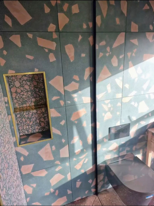 Contemporary bathroom featuring Chunks ROCK Terrazzo Green 60 × 60cm terrazzo-effect porcelain wall tiles, showcasing oversized blush pink aggregate detailing, paired with dark sanitaryware and warm natural sunlight.