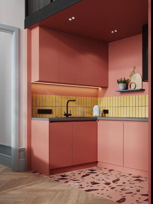 Contemporary pink kitchen featuring Chunks ROCK terrazzo effect porcelain floor tiles in a 60cm x 60cm format, paired with coral pink cabinetry, mustard vertical brick splashback tiles, black worktops and brass accents for a bold, playful interior.