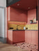 Contemporary pink kitchen featuring Chunks ROCK terrazzo effect porcelain floor tiles in a 60cm x 60cm format, paired with coral pink cabinetry, mustard vertical brick splashback tiles, black worktops and brass accents for a bold, playful interior.