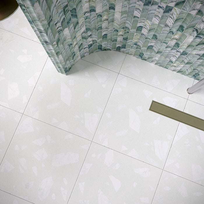 Bathroom featuring Chunks Rock Terrazzo White 60x60cm terrazzo-effect porcelain wall and floor tiles, styled with a curved shower wall, green patterned feature tiles, brushed brass fixtures and soft contemporary décor.