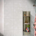 Bathroom featuring Chunks Rock Terrazzo White 60x60cm terrazzo-effect porcelain wall and floor tiles, styled with a curved shower wall, green patterned feature tiles, brushed brass fixtures and soft contemporary décor.