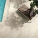 Poolside setting featuring Cocoon Stone Light 2cm 60 × 90cm porcelain tiles, showcasing soft light stone effect tones with gentle veining. Laid in a clean grid, the tiles create a bright, refined surface, complemented by dappled light, water reflections, and contemporary outdoor furniture.