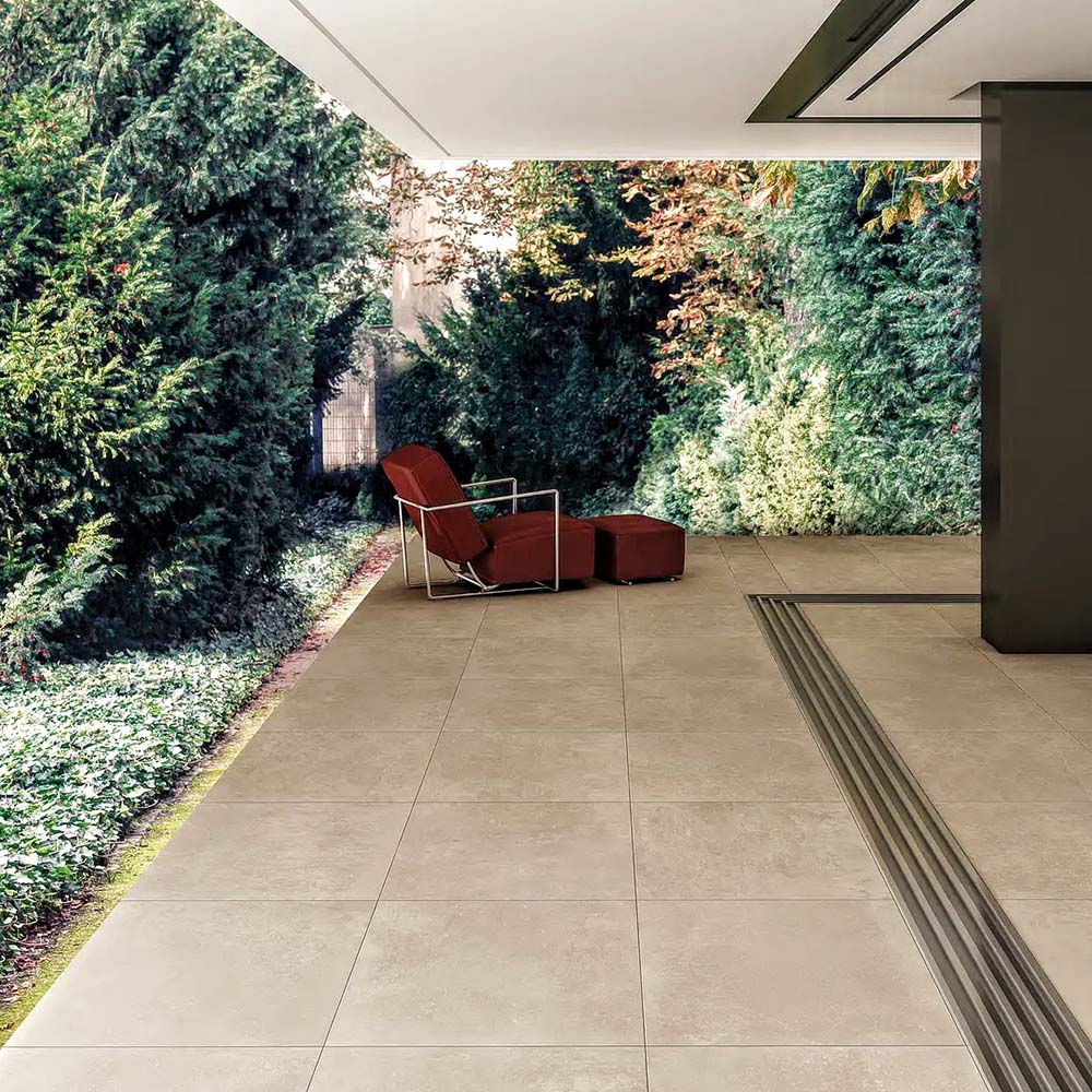Outdoor terrace featuring Cocoon Stone Natural 2cm 60 × 90cm porcelain tiles, laid in a clean grid pattern. Warm natural stone effect tones create a calm, grounded look, complemented by surrounding greenery and contemporary outdoor seating for a seamless indoor-outdoor feel.