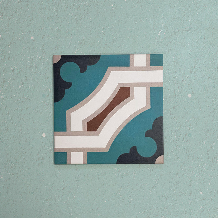Single Europa Cologne 20x20cm Victorian Moroccan style tile displayed against a textured aqua background, featuring a decorative geometric corner pattern in teal, brown, cream and dark blue tones in a close-up product setting.