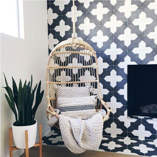 Alhambra Cathedral 20x20cm Moroccan tiles featured in a cozy corner with a hanging wicker chair, neutral cushions, and a modern fireplace — showcasing the bold black and white cross pattern for stylish contemporary interiors.