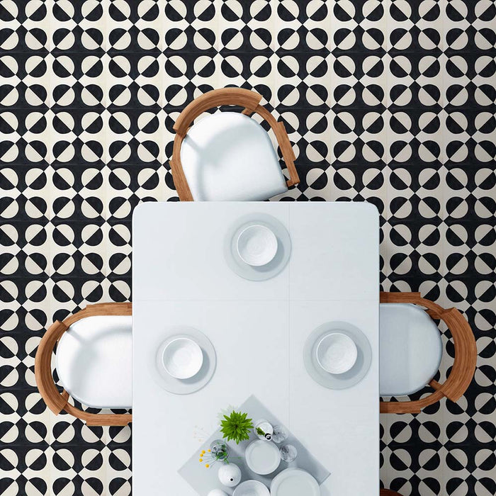 Dining room featuring Geometry Illusion Noir 20x20cm geometric patterned floor tiles in black and cream, styled with a white dining table, wooden-framed chairs, and minimalist tableware.