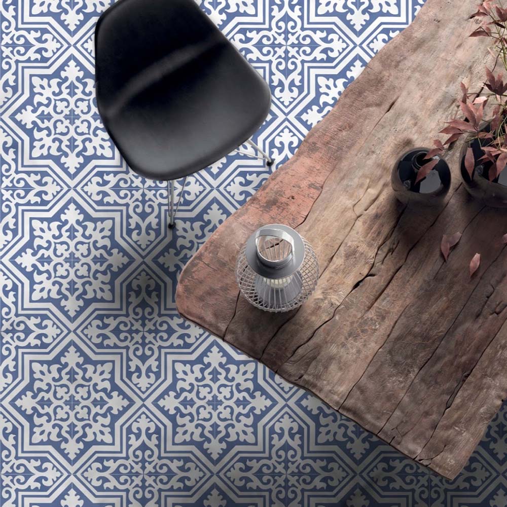 Dining room interior featuring Europa Trondheim Blue 20x20cm Victorian Moroccan style floor tiles in blue and white tones, styled with a rustic wooden table, black chair and decorative accessories in a contemporary interior setting.