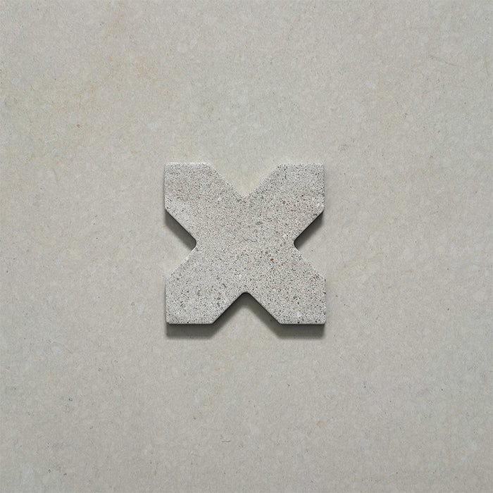 Close-up of a single Dohar Avorio Rocks Cross porcelain wall and floor tile, showcasing its geometric cross shape, soft ivory tone, fine speckled detail and textured matt finish.