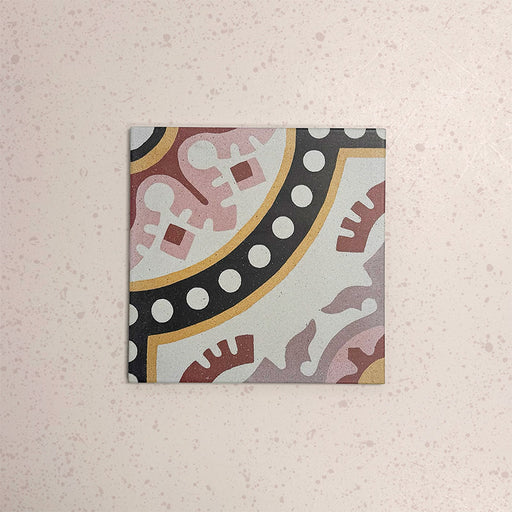 Single Europa Dortmund 20x20cm Victorian Moroccan style tile displayed against a textured blush background, featuring a decorative geometric and floral corner pattern in red, cream, black and mustard tones in a close-up product setting.