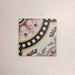 Single Europa Dortmund 20x20cm Victorian Moroccan style tile displayed against a textured blush background, featuring a decorative geometric and floral corner pattern in red, cream, black and mustard tones in a close-up product setting.
