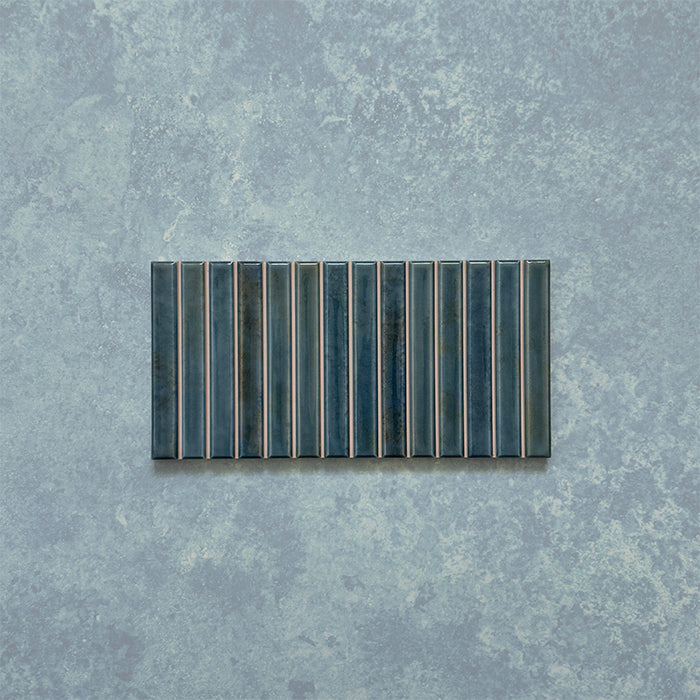 Product display of Elazar Decor Prussian 12.5x25cm ceramic wall tiles in deep blue tones, featuring a linear fluted design, handcrafted glossy finish and subtle tonal variation for textured contemporary interiors.