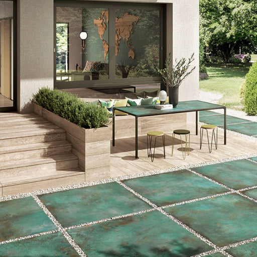 Outdoor patio featuring Elements Oxide 2cm thick porcelain floor tiles in a metallic effect finish, styled with contemporary garden furniture, timber-effect steps, built-in planters and modern landscaping for a luxurious outdoor living space.