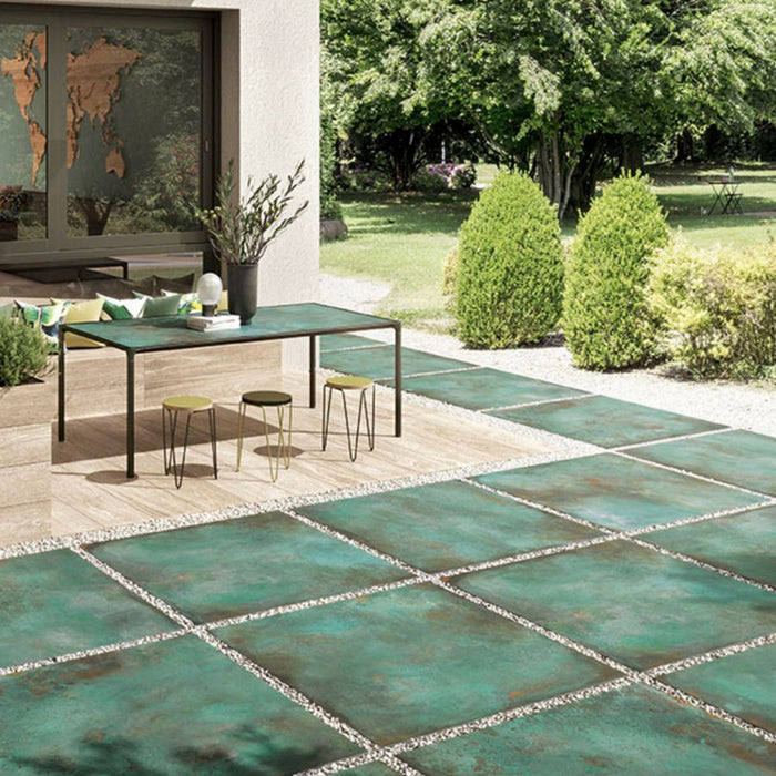 Outdoor patio featuring Elements Oxide 2cm thick porcelain floor tiles in a metallic effect finish, styled with contemporary garden furniture, timber-effect steps, built-in planters and modern landscaping for a luxurious outdoor living space.