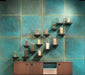 Contemporary interior featuring Elements Oxide 60cm x 60cm metallic effect wall tiles, paired with timber cabinetry and minimalist shelving to create a striking industrial-inspired feature wall with rich blue-green tones.