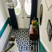 Entryway featuring Sloane Square Black and White 25x25cm Victorian-style ceramic floor tiles, arranged in a traditional geometric pattern with a matching border, styled with teal walls, a wooden side table, and a glass pendant light.
