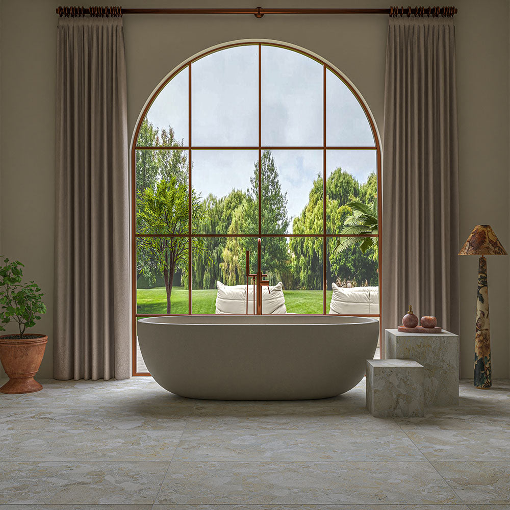 Luxury bathroom featuring Essenza Pura 3D Terrazzo Style Tiles 60cm x 120cm on the floor, styled with a freestanding bath, an oversized arched window, soft neutral décor and warm natural light.
