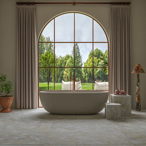 Luxury bathroom featuring Essenza Pura 3D Terrazzo Style Tiles 60cm x 120cm on the floor, styled with a freestanding bath, an oversized arched window, soft neutral décor and warm natural light.