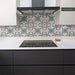 Contemporary kitchen featuring Europa Budapest 20x20cm Victorian and Moroccan-style patterned splashback tiles, with intricate green, grey and white floral geometric motifs, paired with dark grey cabinetry, white worktops and a black hob.