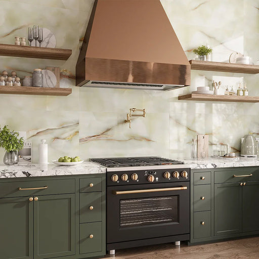 Kitchen interior featuring Fantasia Jade Green Onyx Polished 60 × 120cm stone effect wall tiles, with soft green tones and flowing gold veining, paired with green cabinetry, marble worktops, and a copper extractor hood.