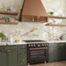 Kitchen interior featuring Fantasia Jade Green Onyx Polished 60 × 120cm stone effect wall tiles, with soft green tones and flowing gold veining, paired with green cabinetry, marble worktops, and a copper extractor hood.