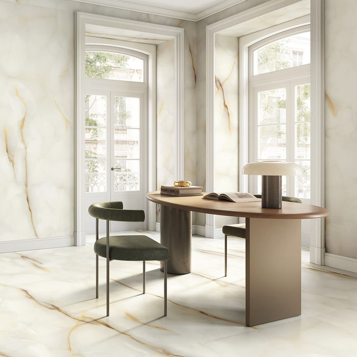 Dining space featuring Fantasia Pearl Onyx Silk Matt 60 × 120cm stone effect floor and wall tiles, with soft cream tones and delicate gold veining, paired with a wooden table, upholstered chairs, and large arched windows.