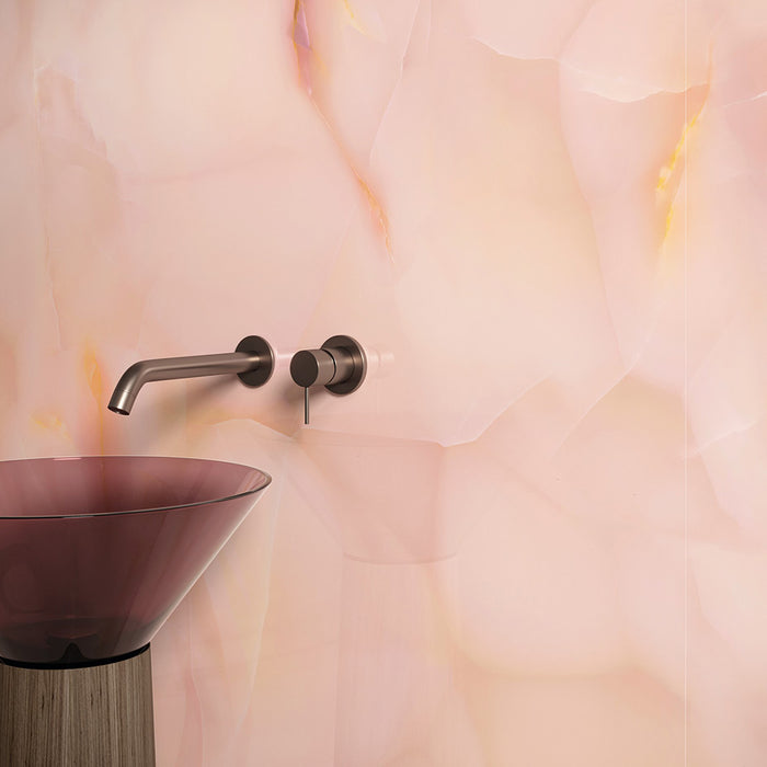 Bathroom detail featuring Fantasia Rose Onyx Matt 60 × 120cm stone effect wall tiles, showcasing soft blush pink tones with subtle gold veining, paired with a smoked glass basin and brushed metal wall-mounted tap for a warm, contemporary finish.