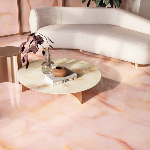 Living space featuring Fantasia Rose Onyx Polished 60 × 120cm stone effect floor tiles, showcasing soft blush pink tones with delicate gold veining, paired with a curved cream sofa, sculptural coffee table, and warm metallic accents for a refined finish.