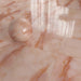 Flat lay of Fantasia Rose Onyx Polished 60 × 120cm stone effect floor tiles, arranged in a grid layout to showcase soft blush pink tones, glossy finish, and flowing gold veining, styled with a matching decorative sphere to highlight the tile’s reflective surface and depth.