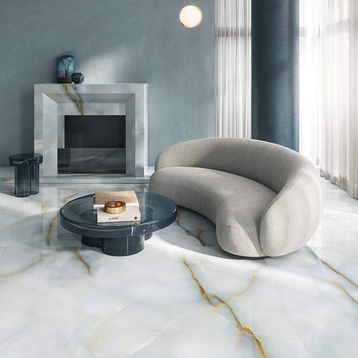 Living room interior featuring Fantasia Turchese Blue Onyx Matt 60 × 120cm stone effect floor tiles, showcasing soft blue-grey tones with flowing gold veining, paired with a curved neutral sofa, glass coffee table, and minimalist fireplace for a calm, contemporary finish.