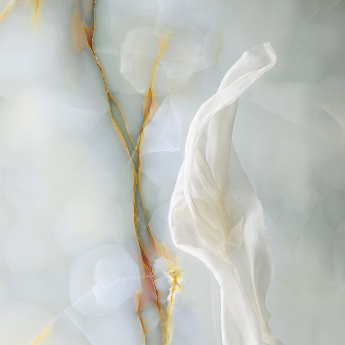 Styled flat lay of Fantasia Turchese Blue Onyx Matt 60 × 120cm stone effect tile, showcasing soft blue-grey tones with flowing gold veining, paired with draped sheer fabric to highlight the tile’s gentle texture, depth, and softly diffused finish.