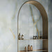 Bathroom interior featuring Fantasia Turchese Blue Onyx Polished 60 × 120cm stone effect wall tiles, showcasing soft blue-grey tones with striking gold veining, paired with an arched metallic shelving niche and warm-toned accessories for a refined, contemporary finish.