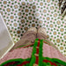 Cabana Tanane Moroccan Style 20x20cm tiles shown in a real-life setting from above, featuring a geometric star and cross pattern in green, pink, white, and tan tones beneath a person wearing beige trousers and cream shoes