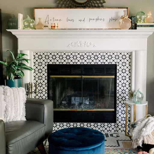 Living room featuring Agraba Black and White Mini 15x15cm Moroccan-style ceramic tiles framing a traditional fireplace, styled with neutral décor, plush textiles, and a navy velvet footstool for a cosy modern look.