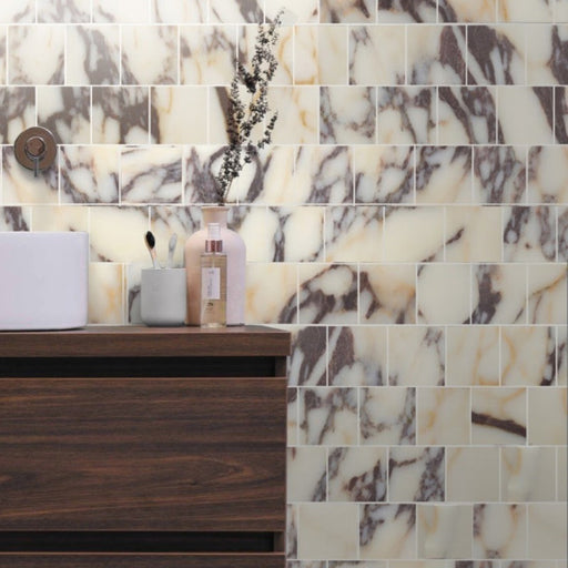 Contemporary bathroom featuring Fitzrovia Calacatta Viola honed natural marble mosaic wall tiles in a brick pattern, showcasing dramatic purple and warm gold veining. Styled with a dark wood vanity, countertop basin and minimalist accessories for a luxurious, timeless finish.