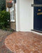 Outdoor entrance featuring Fitzrovia Rosso 15.2cm x 15.2cm natural marble floor tiles with a tumbled finish, laid beside traditional brickwork, a navy front door and surrounding greenery.