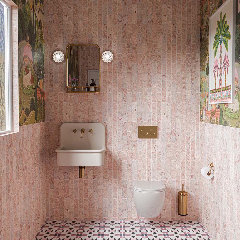 Bathroom featuring Fitzrovia Sylvester Pink 5x20cm honed natural marble wall tiles, with soft blush pink tones and distinctive veining, laid vertically and paired with patterned floor tiles, decorative wallpaper, a white wall-mounted basin and brass fittings.