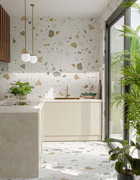 Kitchen featuring Fragmenta Light 60cm x 120cm terrazzo effect porcelain wall and floor tiles, showcasing a light neutral base with scattered multicoloured stone-style fragments, paired with white cabinetry, brass details and greenery.