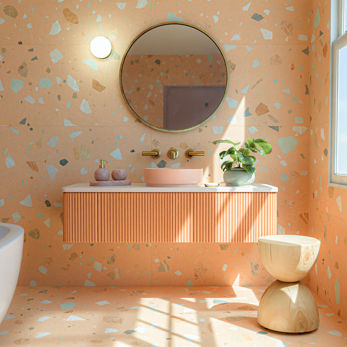 Bathroom featuring Fragmenta Terracotta 60cm x 120cm terrazzo effect porcelain wall and floor tiles, showcasing warm terracotta tones with scattered multicoloured stone-style fragments, paired with a fluted vanity, brass fixtures and greenery.