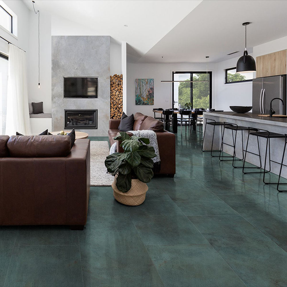 Open-plan living and kitchen space featuring Furnace Emerald Green Oxide Metallic 30 × 60cm porcelain floor tiles, showcasing rich green tones with subtle tonal variation and a soft metallic effect, paired with warm leather seating, natural wood, and modern black accents for a bold yet balanced contemporary interior.
