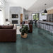Open-plan living and kitchen space featuring Furnace Emerald Green Oxide Metallic 30 × 60cm porcelain floor tiles, showcasing rich green tones with subtle tonal variation and a soft metallic effect, paired with warm leather seating, natural wood, and modern black accents for a bold yet balanced contemporary interior.