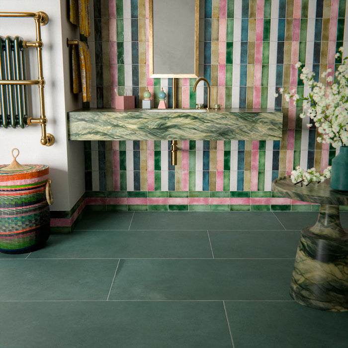 Bathroom interior featuring Furnace Emerald Green Oxide Metallic 60 × 120cm porcelain floor tiles, styled with rich green tones and soft tonal variation, paired with a colourful striped feature wall, brass fittings, and a marble-effect vanity for a bold, design-led finish.
