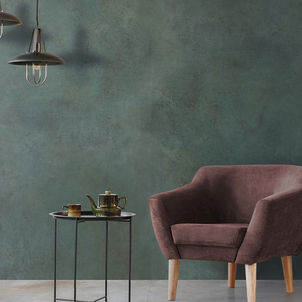 Living space detail featuring Furnace Emerald Green Oxide Metallic 60 × 60cm porcelain wall tiles, showcasing deep green tones with subtle tonal variation and a soft metallic effect, paired with warm upholstery, light wood legs, and minimal styling for a calm, contemporary contrast.