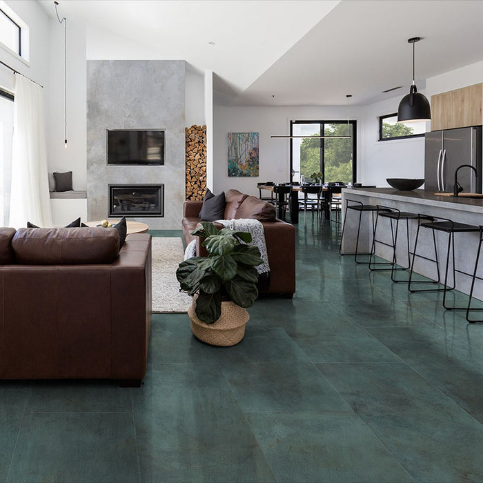 Open-plan living and kitchen space featuring Furnace Emerald Green Oxide Metallic 60 × 60cm porcelain floor tiles, showcasing rich green tones with subtle tonal variation and a soft metallic effect, paired with warm leather seating, natural wood, and modern black accents for a bold yet balanced contemporary interior.