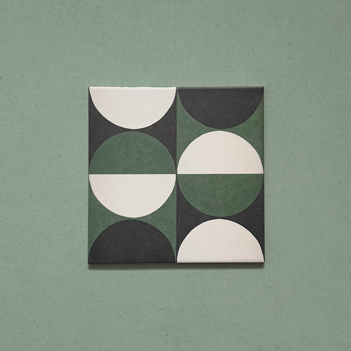 Single tile image showing the Geometry Circulo 20x20cm geometric patterned tile with green, black, and cream semicircle motifs, photographed against a soft green textured background.